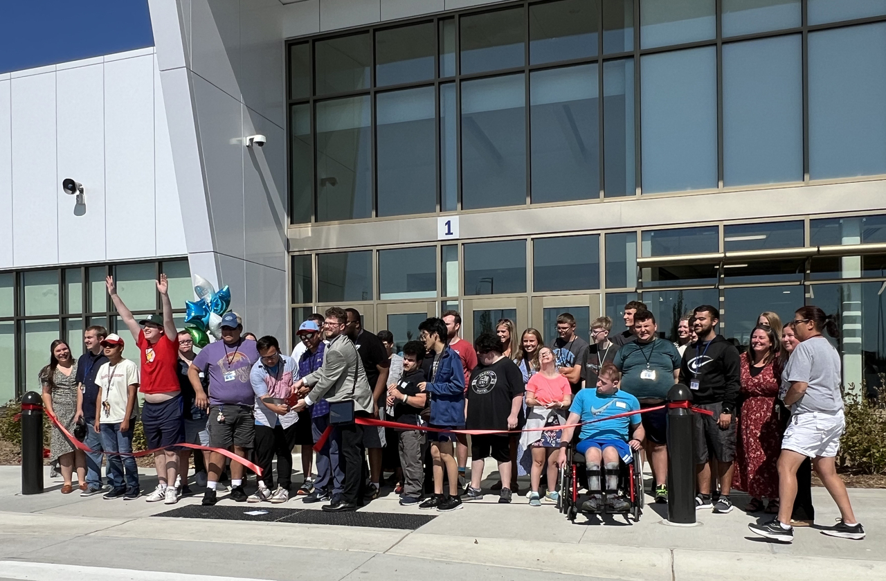 Group of students in front of new Young Adult Services building cutting ribbon for grand opening